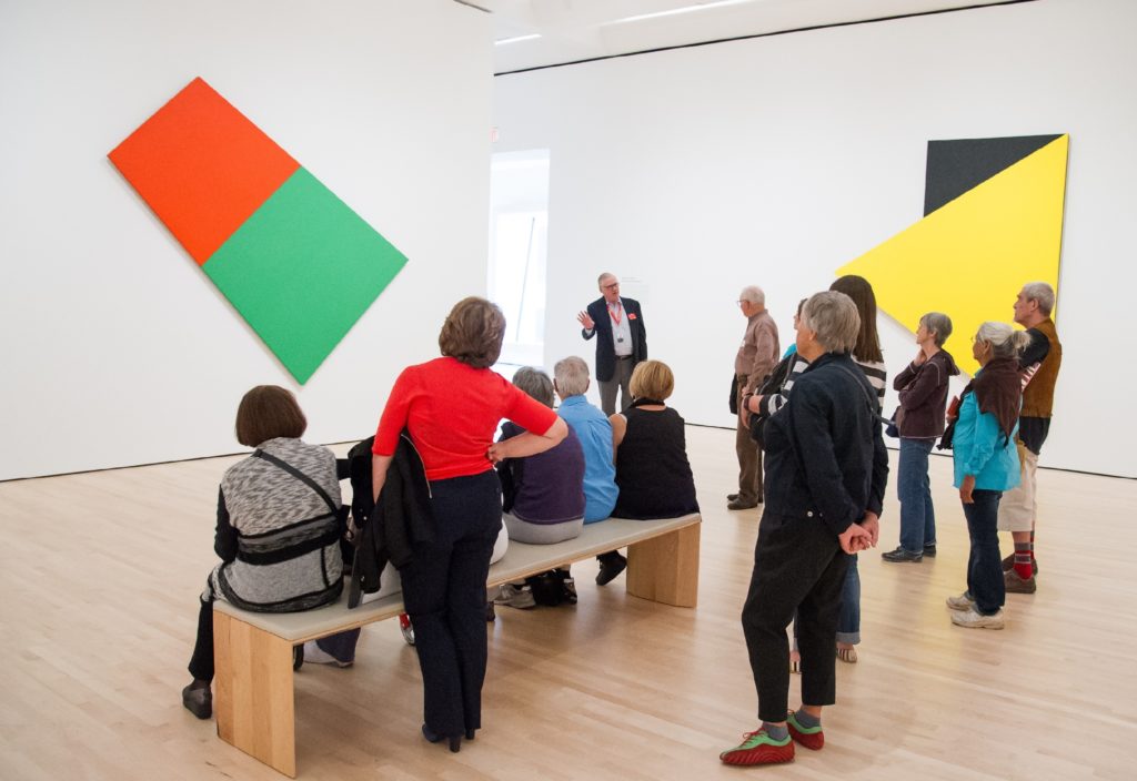 A museum guide soeaks to a group in front of an Ellsworth Kelly painting