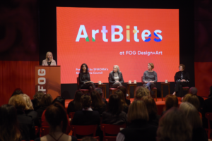 Five women sit on a stage before a large red screen with the words ArtBites