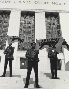 Three men in black leather jackets, hold "Free Huey" banner son the steps of the Oakland courthouse