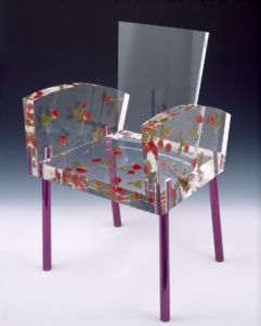 A transparent geometric chair with a red floral pattern on the arms and seat