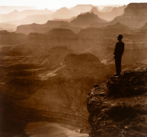 A man in silhouette stands on a cliff overlooking the Grand Canyon