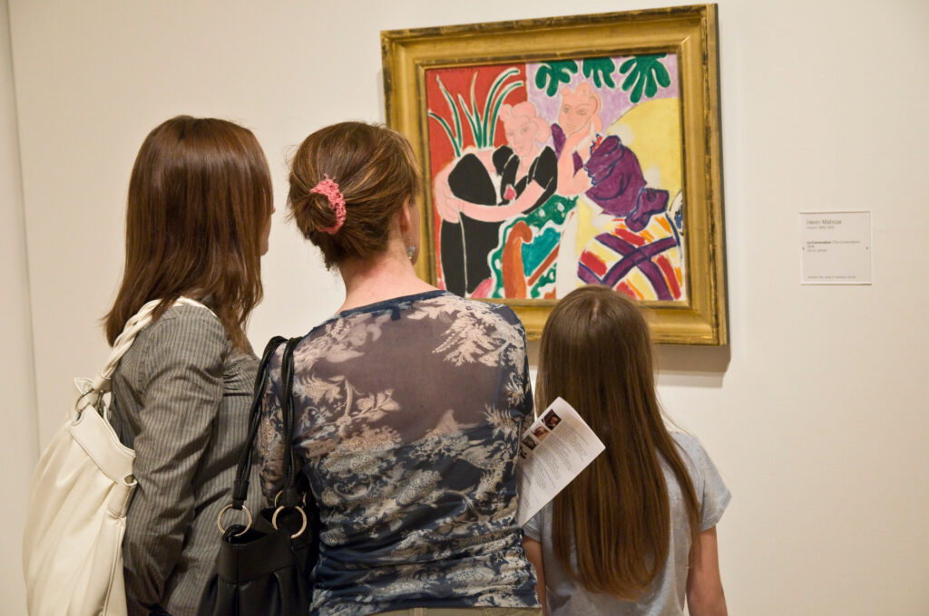 A woman and two girls looks at a colorful painting by Matisse of two women