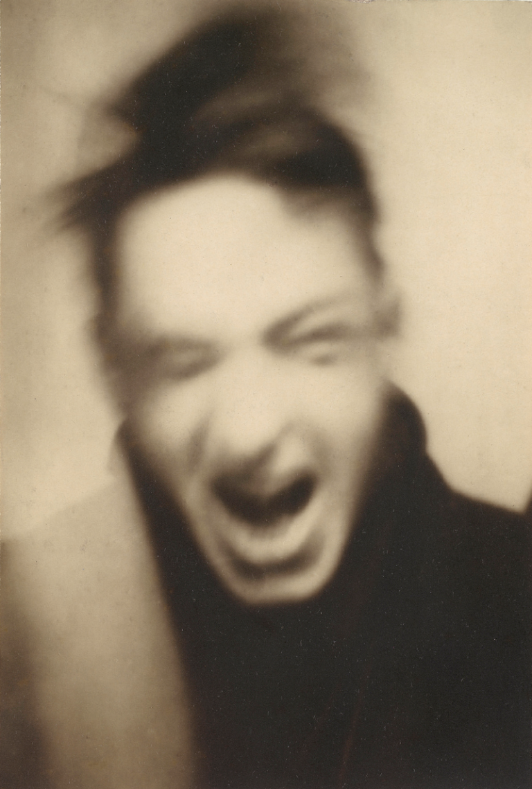 A blurry black and white photograph of a screaming man with disheveled hair