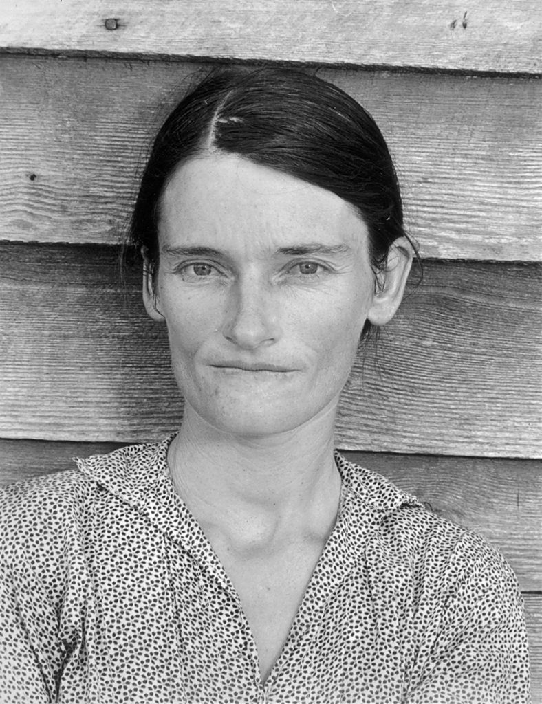 Portrait of a woman with a furrowed brow standing in front of an unpainted wood wall