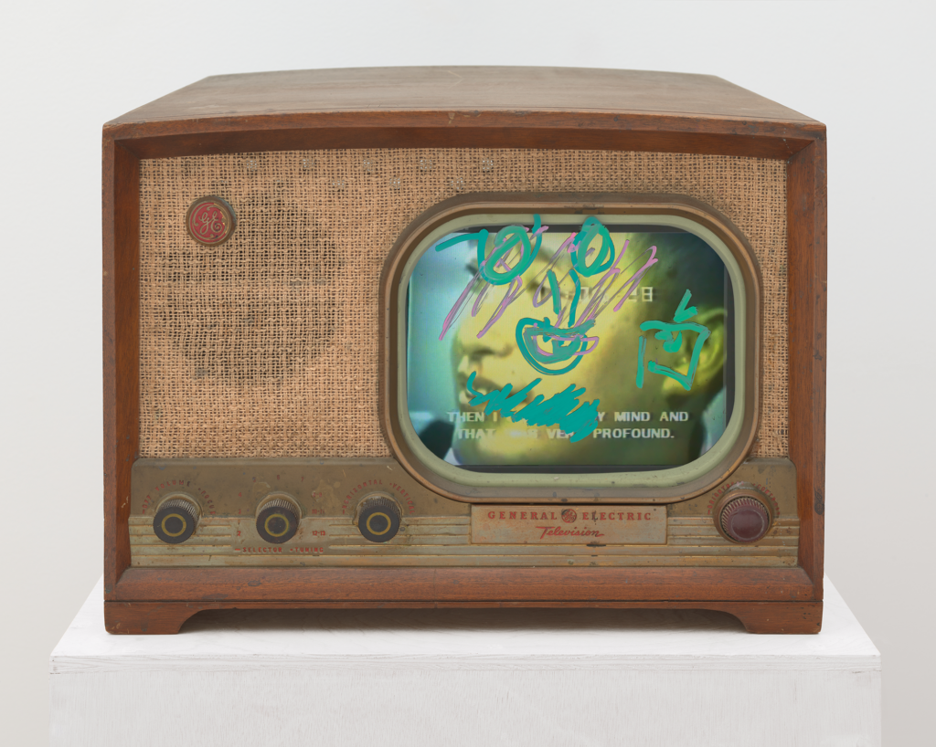 Old-fashioned General Electric television with a screen showing color video painted over with opaque neon scribbles