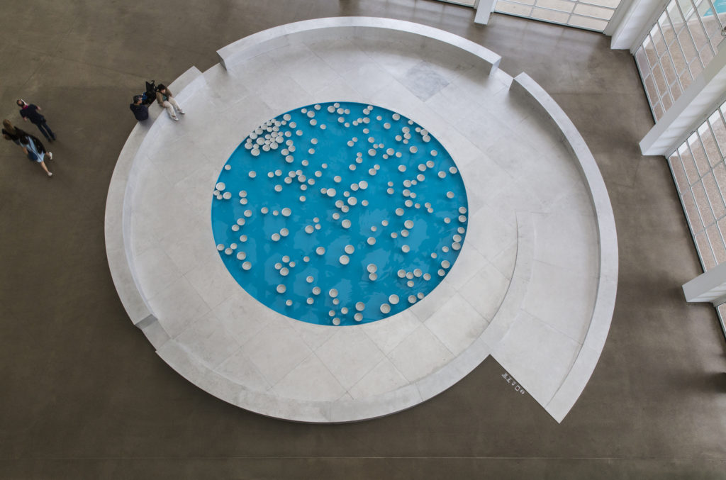 Porcelain bowls float across the surface of a shallow, circular pool filled with turquoise water