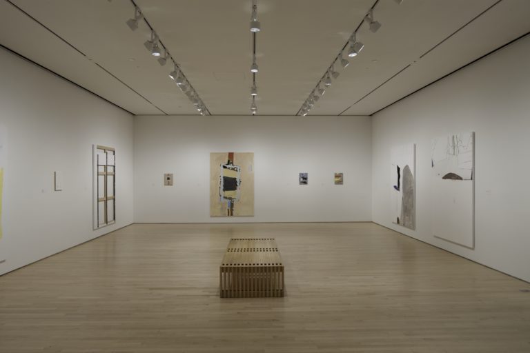 1.)	A white room with a bench in the middle of the room. The white walls have Richard Aldrich’s work on them.