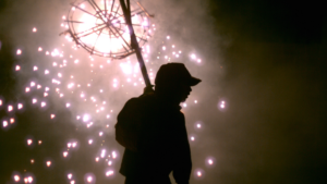 A man in silhouette with bright fireworks behind him