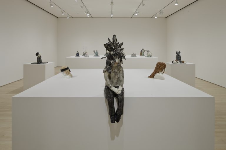 A room with several sculptures, including a ceramic figurine with moths covering its face.