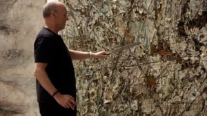 Artist Anselm Kiefer slashes at one of his large, textural paintings with a metal tool.