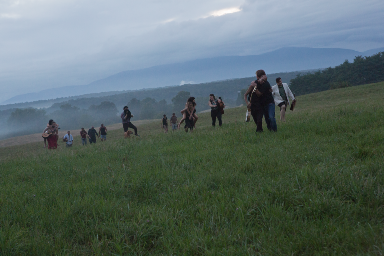 Several people stand in an open green field at dusk, Kjartansson