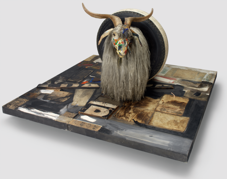 A colorfully painted Angora goat head ina rubber tire atop a wood platform