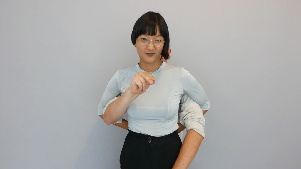 An Asian woman wearing glasses stands in front of a grey background with someone else's arms around her waist, Kim Soundtracks