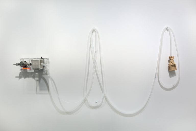 White wall with a machine and a brown paper bag strung together, Lozano-Hemmer Soundtracks