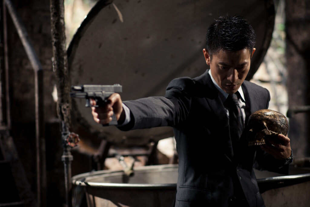 Film still of a man pointing a gun and holding a human skull