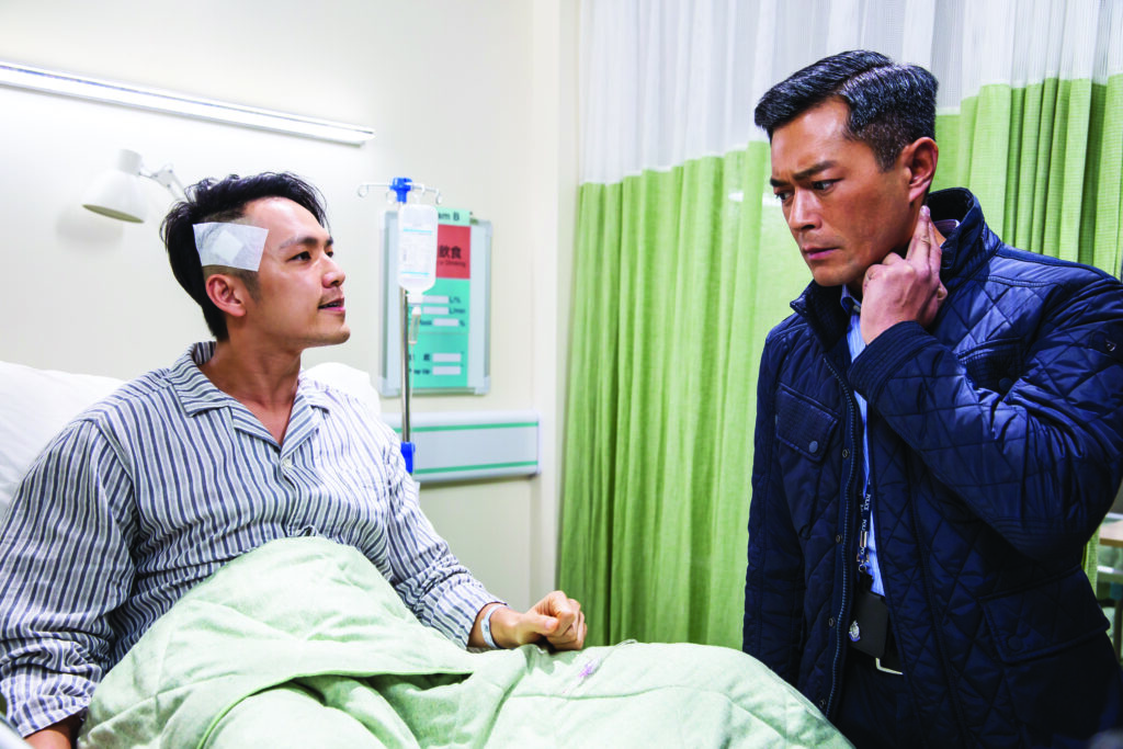A man sits in a hospital bed facing another man