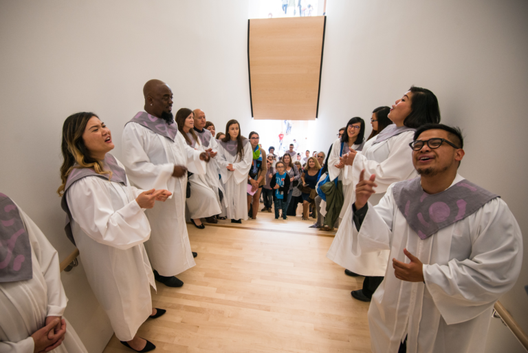 A group of people wearing white robes sing on a staircase, Paradise Choir, Kallmyer, Soundtracks