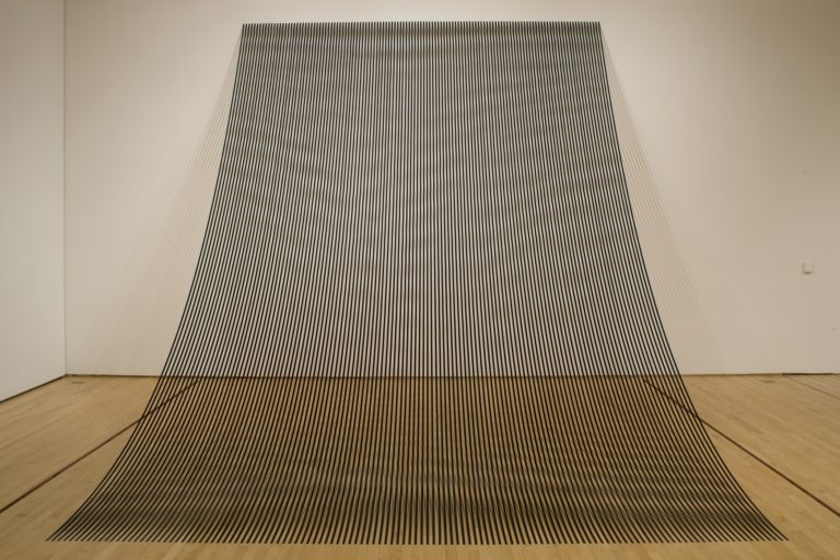A sculpture made up of black strips that drape from the wall onto the floor 