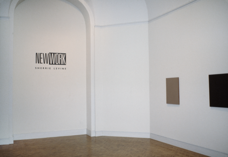 One brown and one black canvas hanging in  a gallery with the words "New Work: Sherrie Levine" on the wall