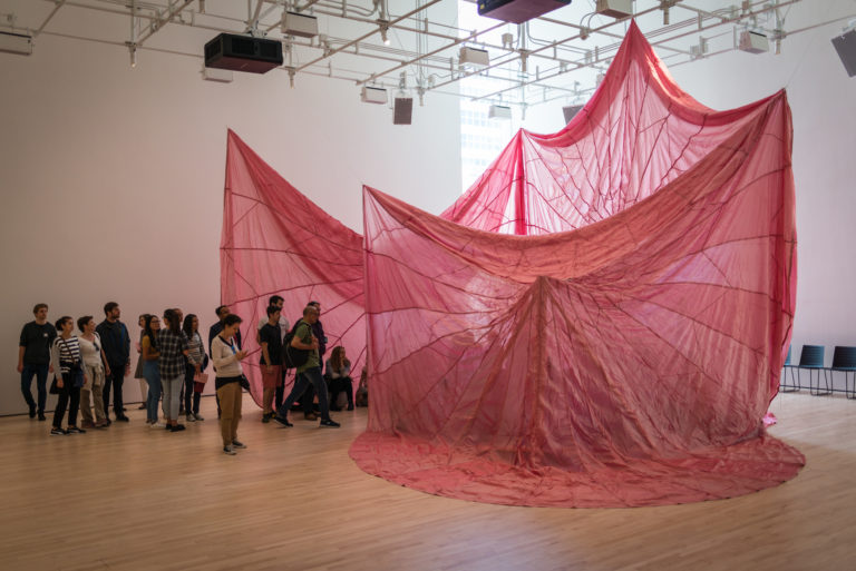 Visitors in the white box looking in between pink hanging fabric