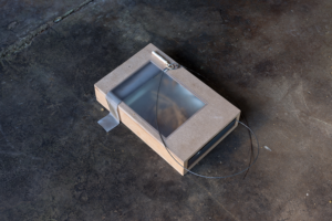 A box with a translucent lid and wire outside on the floor