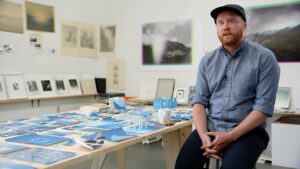 Artist Sean McFarland in his studio, next to a table covered in small blue photographs