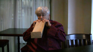 Pauline Oliveros, an older woman, breaths into a paper bag
