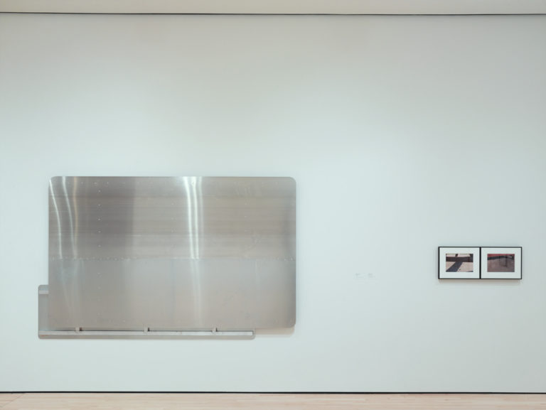 A hung panel of brushed aluminum next to two smaller framed photographs of picnic benches