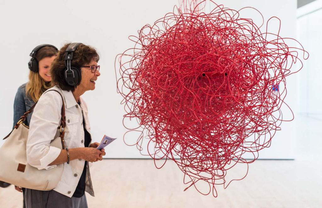 A middle-aged Caucasian woman wearing headphones smiles before a cloud made out of red electrical wires, Kubisch, Soundtracks