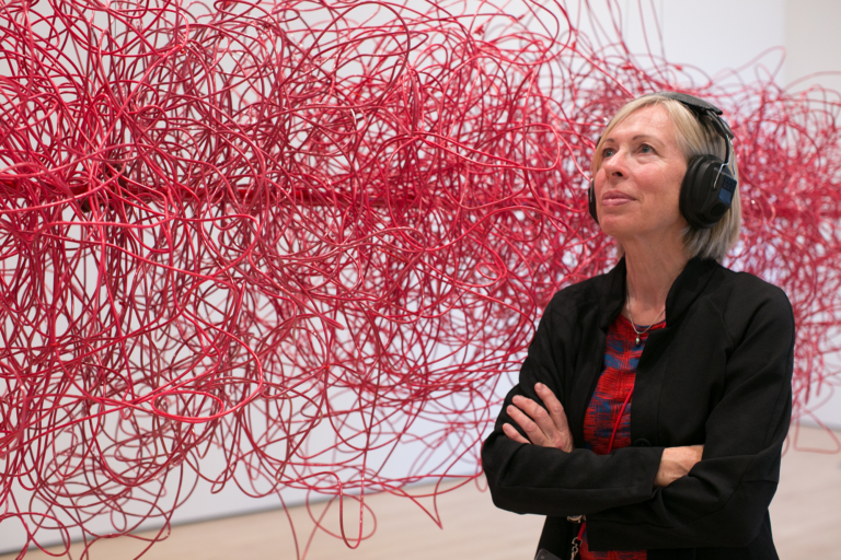 A blond Caucasian woman wears black headphones next to a cloud made of red electrical wires, Kubisch, Soundtracks