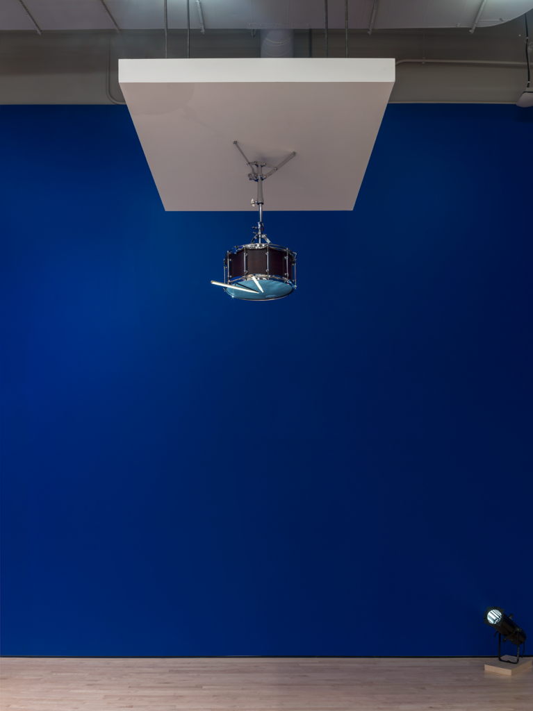 A snare drum hangs from the ceiling before a royal blue wall, Sala, Soundtracks