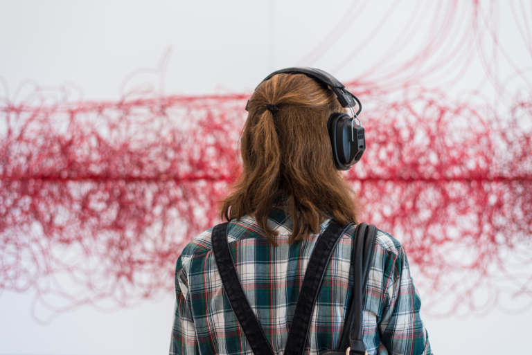 A blond woman wearing headphones looks at a tangled cloud of red chord, Kubisch, Soundtracks