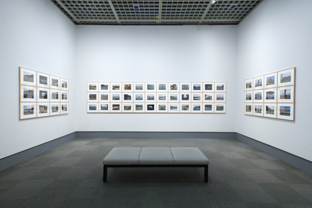 A gallery with a grid of photographs in white frames hanging on the wall, Hatakeyama