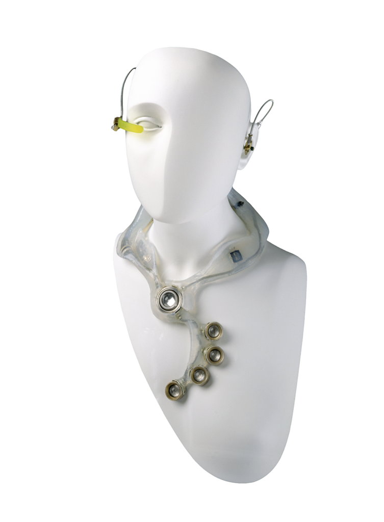 A white mannequin wearing a futuristic wired earpiece and necklace