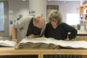 A middle-aged Caucasian man and woman look over an antique manuscript, Public Knowledge