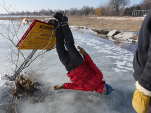 A man leaning upside down on a "no swimming" sign on a frozen lake