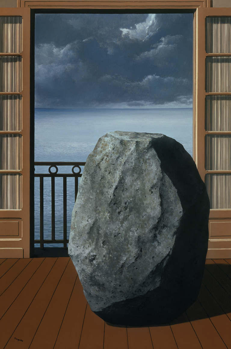A large gray boulder on a wooden floor next to an open door overlooking a veranda with an ocean view