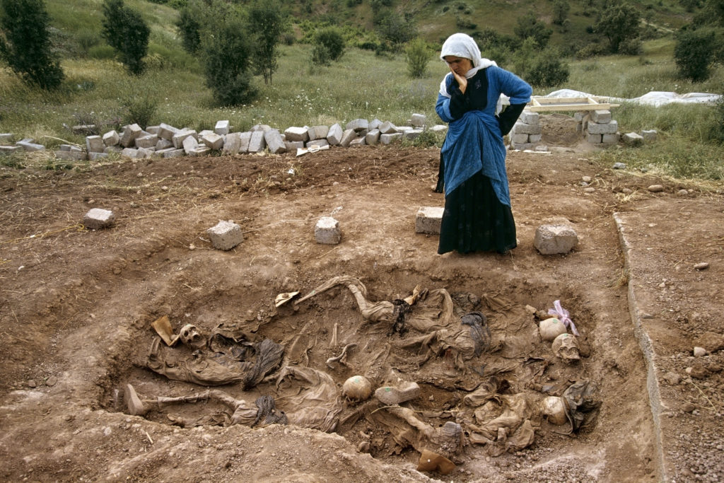 A woman touches her face as she looks down into a mass grave