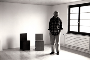 Black and white photograph of a man standing next to square, modernist chairs