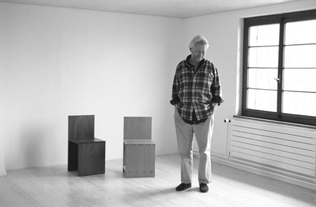 black and white photograph of man standing in room next to chairs - HIGH RES