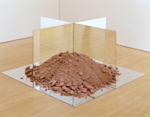 A sculpture of red soil and rocks on top of a mirror bisected by two other mirrors.