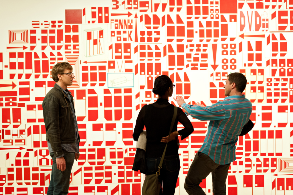 A woman and two men stand in front of a red and white wall installation