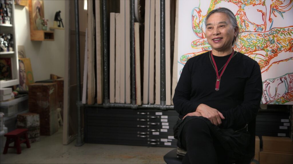 Artist Liu Hung sits in her studio with rows of canvases behind her
