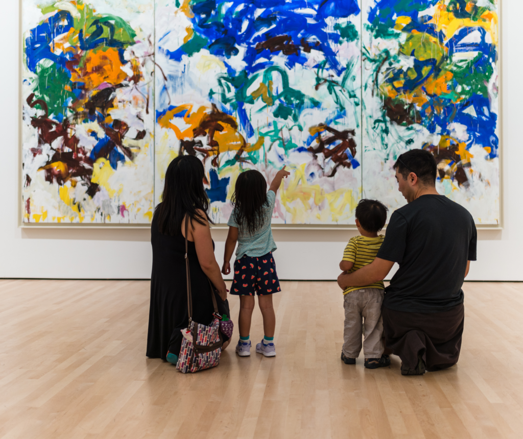 A family kneels looking at a Joan Mitchell painting