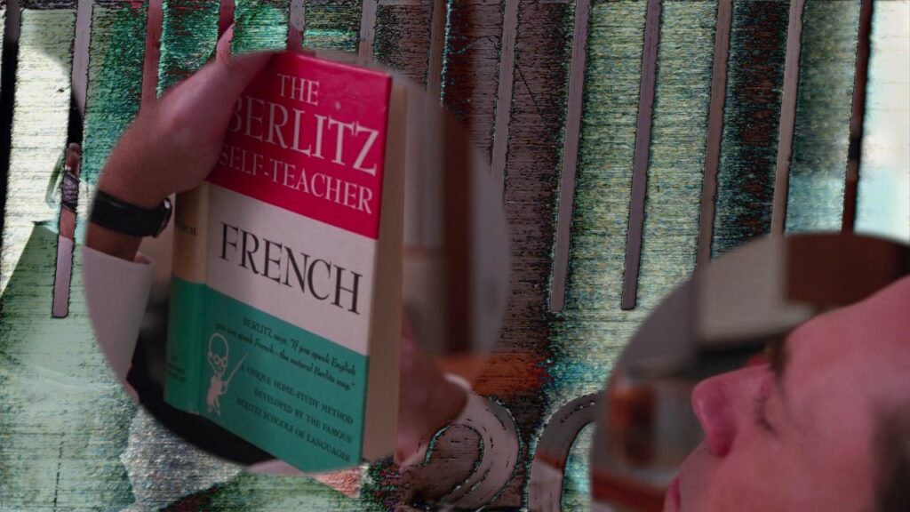 Film still of a man reading "The Berlitz Self-Teacher: French."