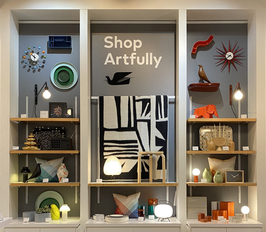 Shelves of unique and colorful home decor items such as clocks, lamps, and vases below a sign that says "Shop Artfully."