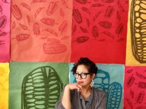 Headshot of Favianna Rodriguez in front of colorful artwork.