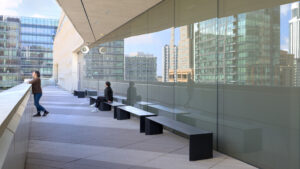 Two people, one sitting and one standing outdoors on the SFMOMA terrace, enjoy the sound installation by artist Susan Philipsz while looking at panoramic views of downtown San Francisco.