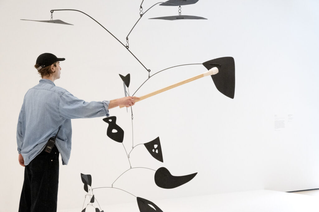 SFMOMA employee interacting with one of Alexander Calder's hanging mobile sculptures to demonstrate how it moves.