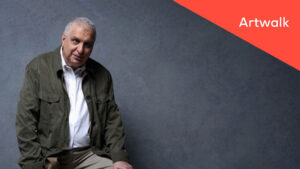 Image of filmmaker Errol Morris sitting in front of a grey background, and the text "Artwalk" in a red triangle at the top right-hand corner of the image.